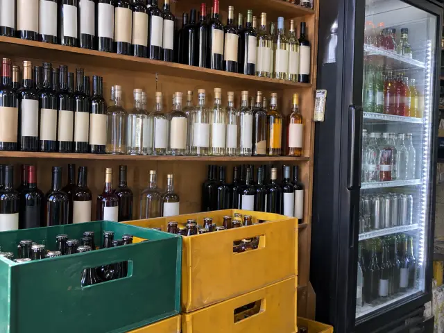 Estantería de botillería con botellas sin etiqueta y cajas de cerveza apiladas
