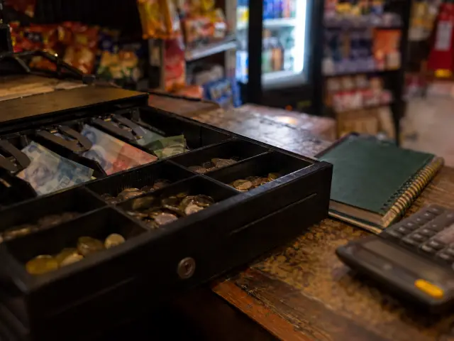 Gaveta de caja abierta con billetes desenfocados, cuaderno y calculadora al cierre del día