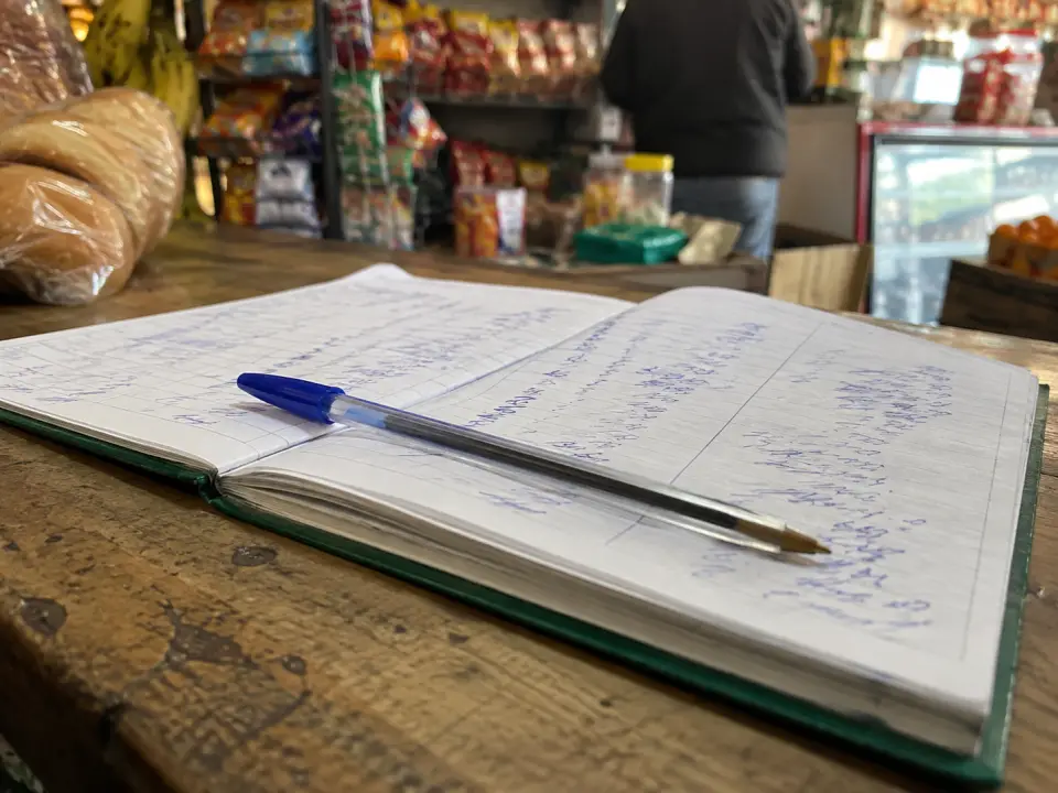 Cuaderno escolar abierto con columnas del fiado escritas a mano sobre un mostrador de madera